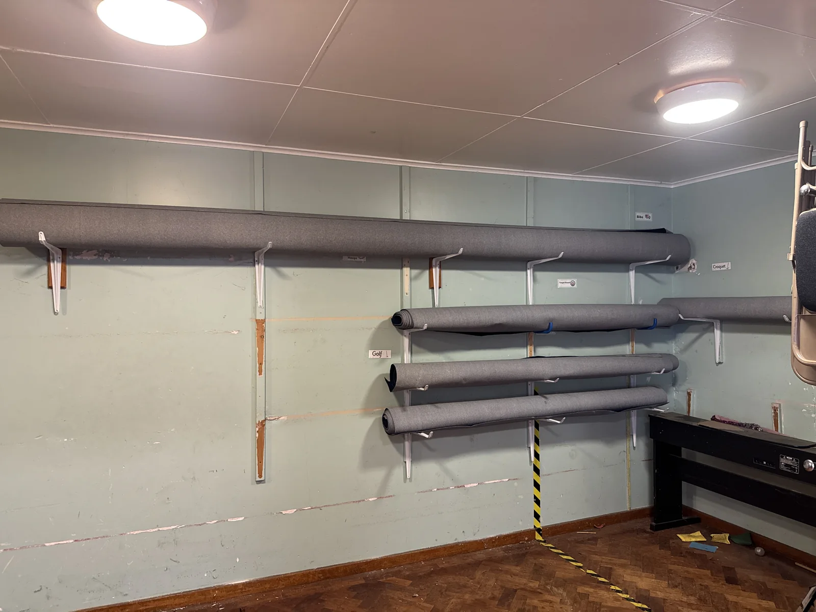 Lengths of grey RC track carpet cut to size and stored horizontally on wall-mounted brackets at Heymann Primary School